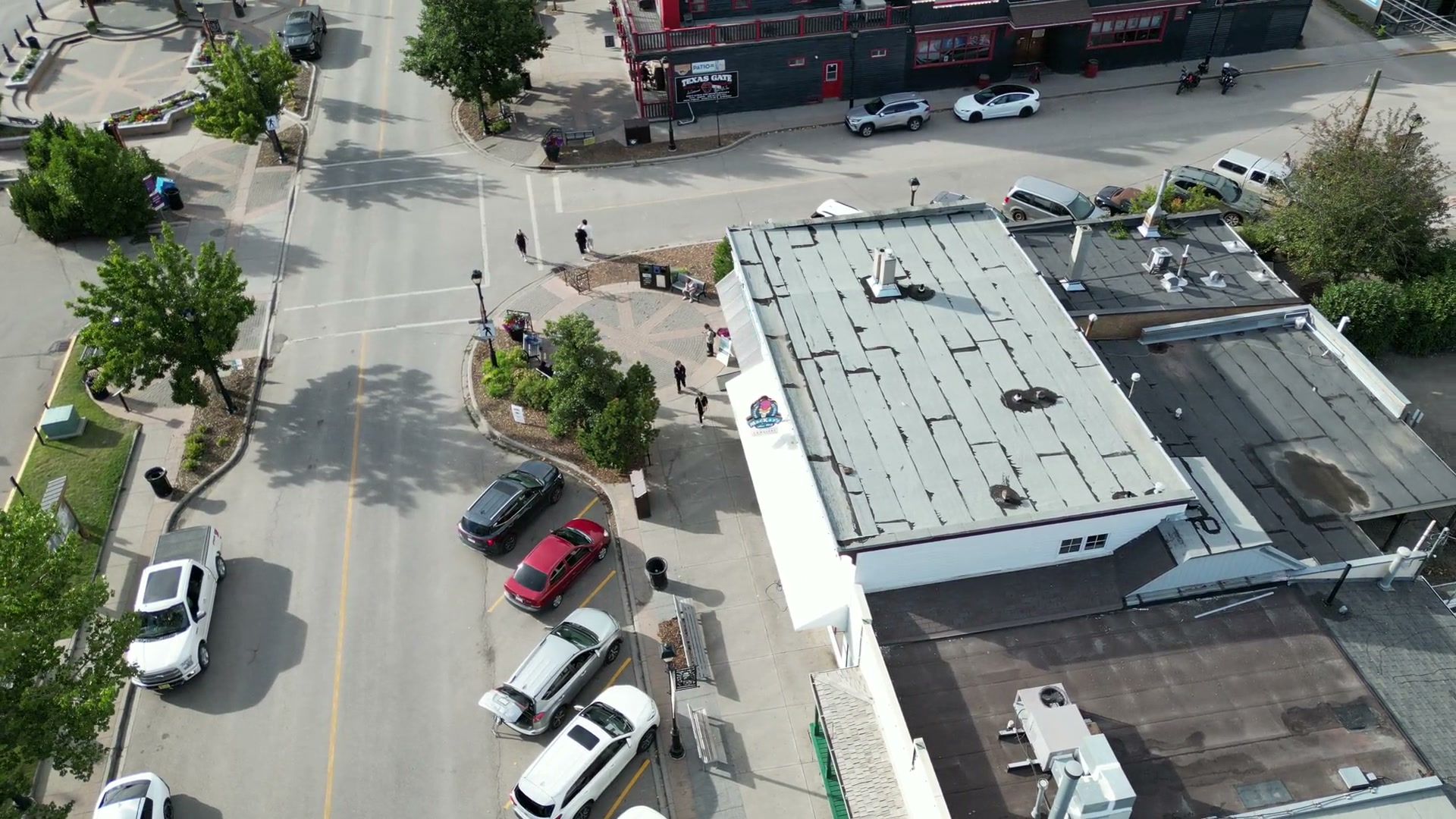 The shop's roof and awning from high above, the sign on its wall and cars angled along 1st Street West