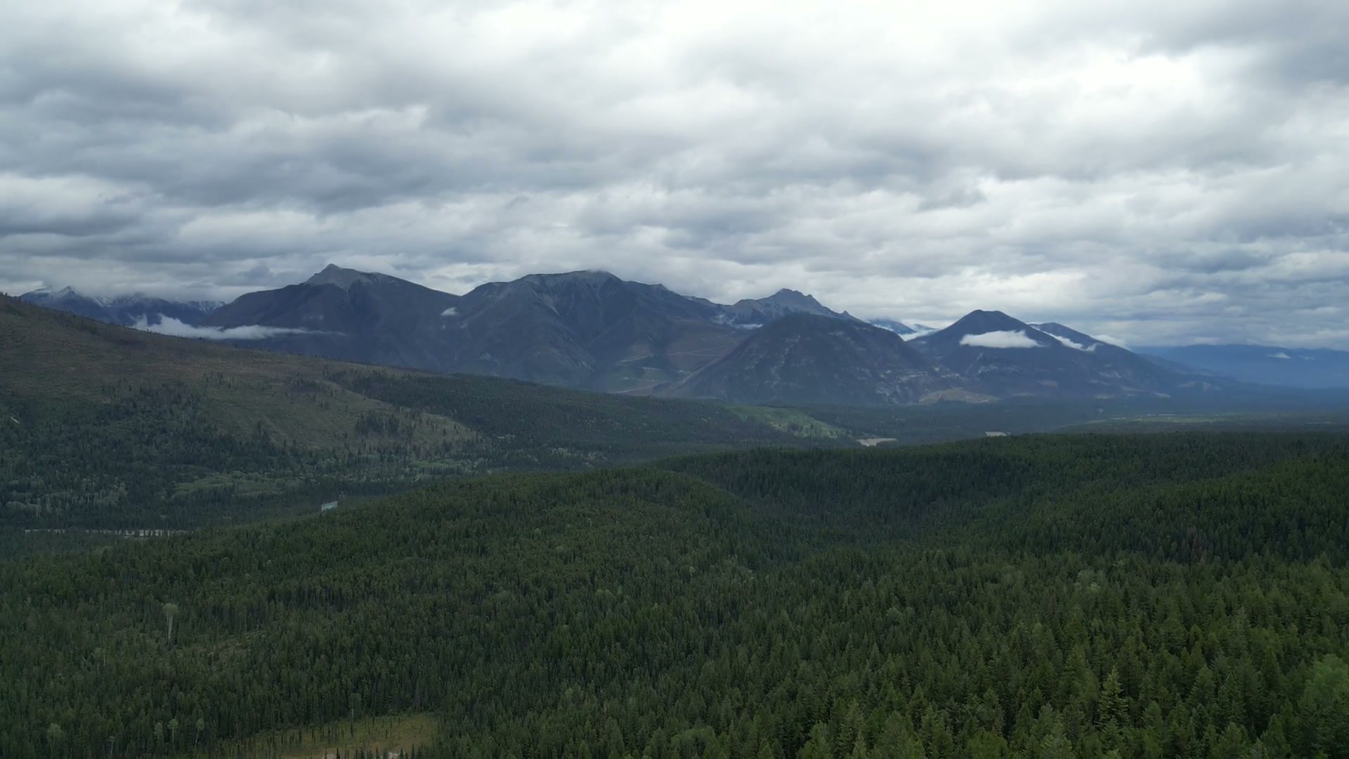 Turning away from the road over dark unbroken forest at Radium Hot Springs toward a range of mountains under heavy cloud, the valley opening to the left