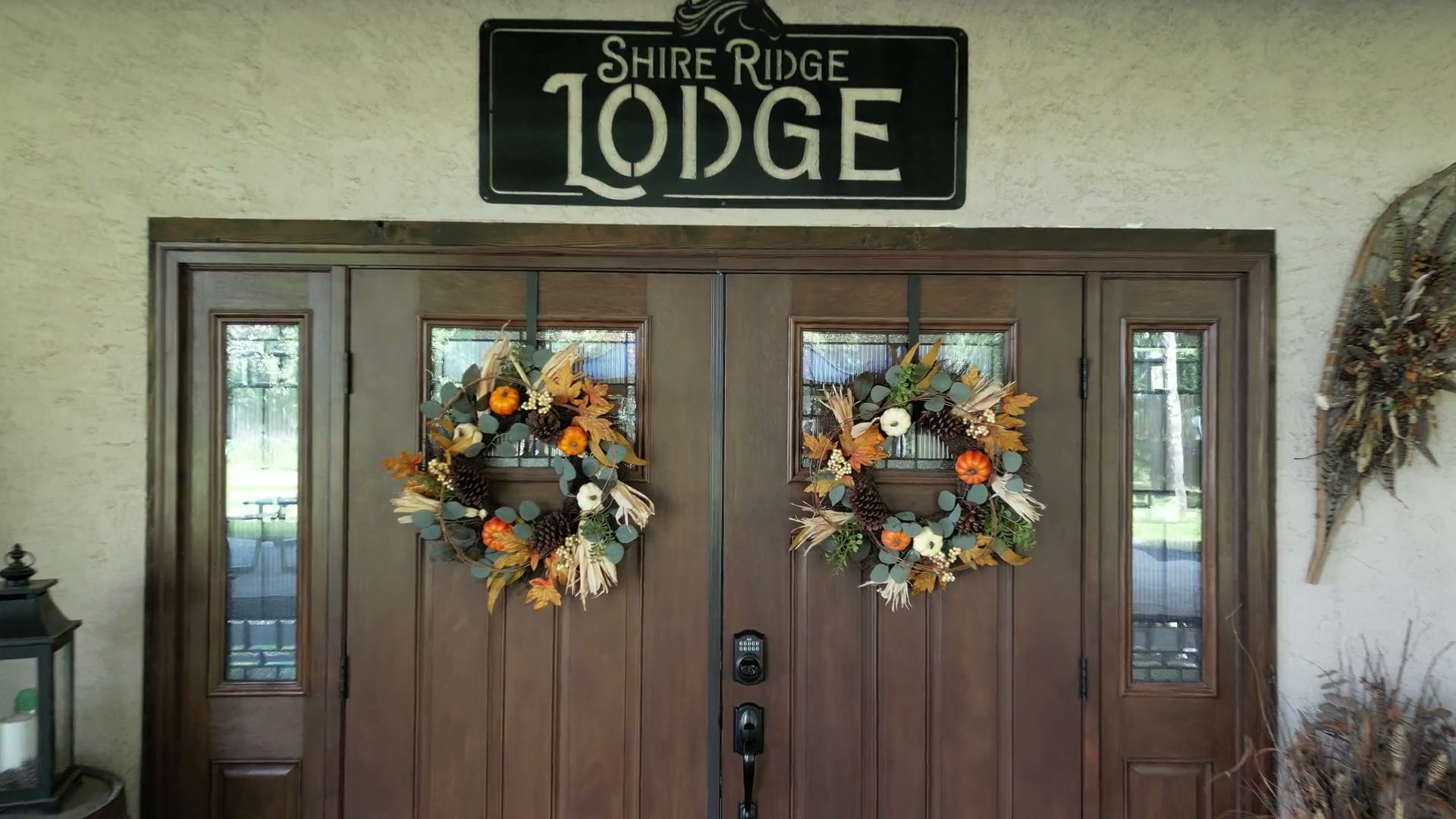 Pushing in at the front of Shire Ridge Lodge near Bragg Creek toward the sign over its double doors, autumn wreaths of pumpkins and pinecones on both, lanterns and wooden barrels beside them
