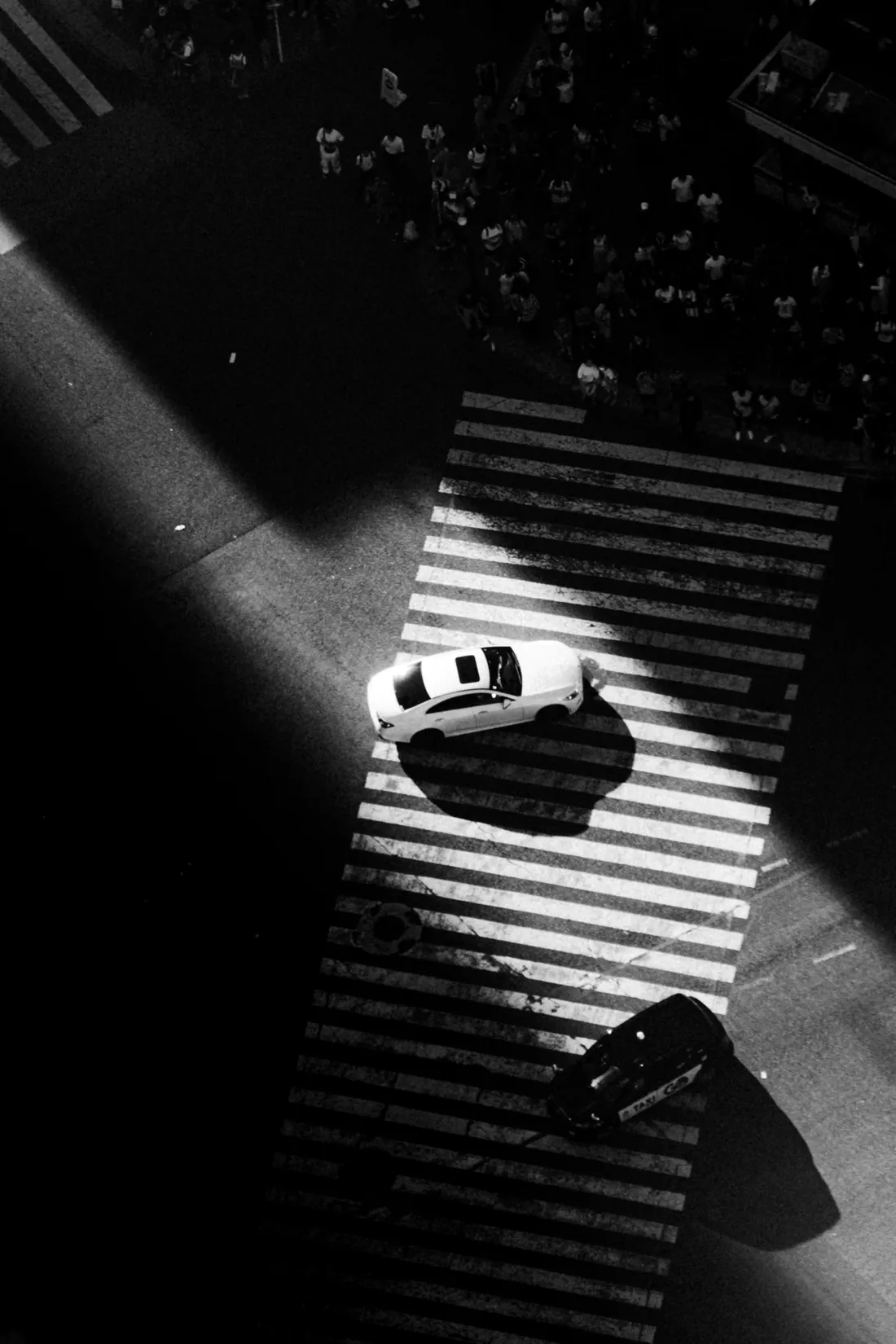 A white car crossing a striped crosswalk seen from directly above in black and white