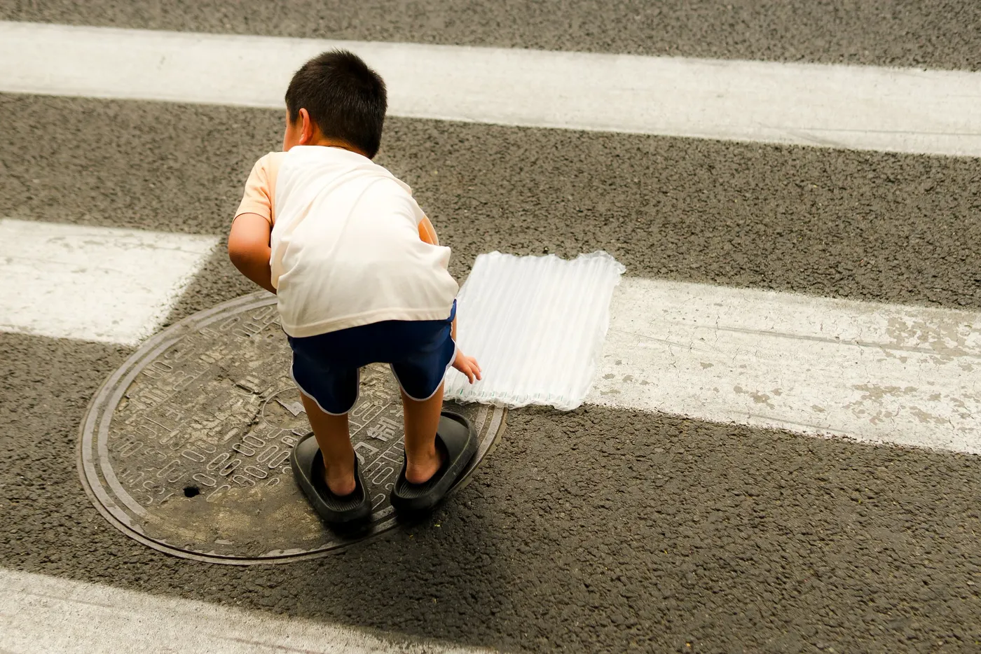 A child crouching on a manhole cover in the middle of a painted crosswalk