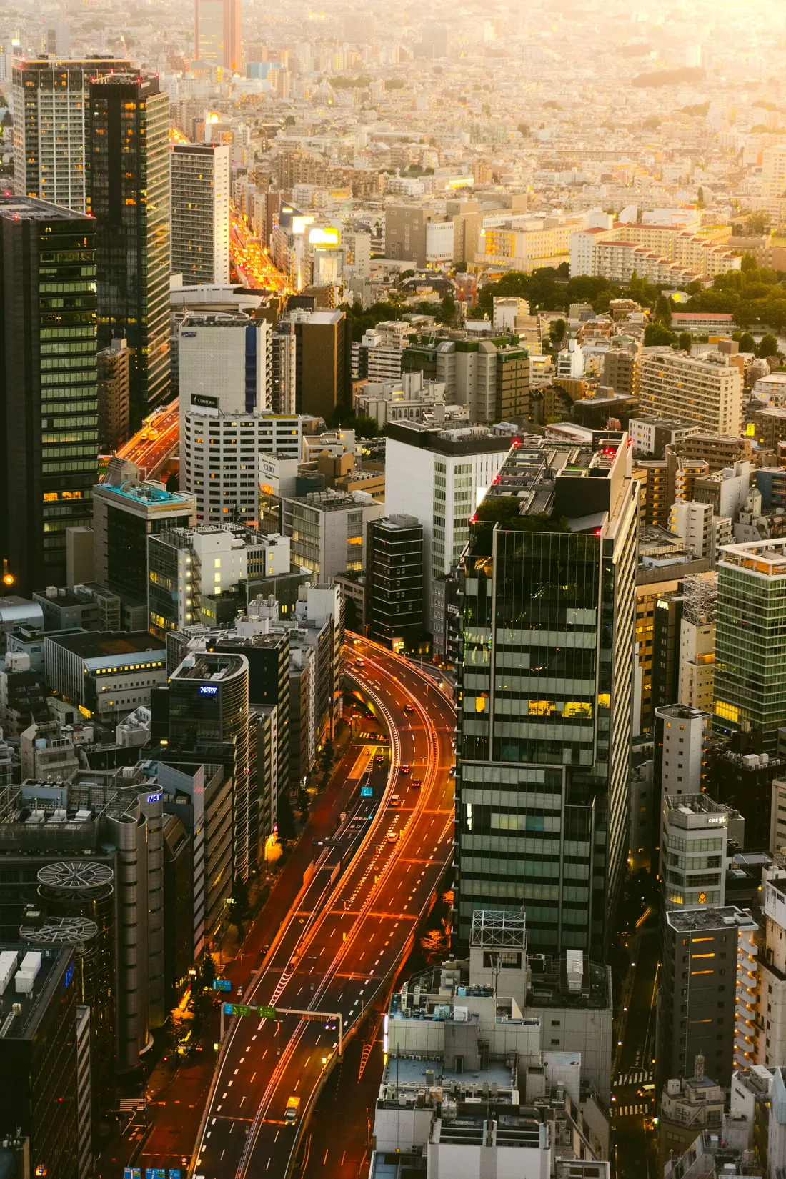 An expressway threading through a dense city at dusk, tail lights drawn out