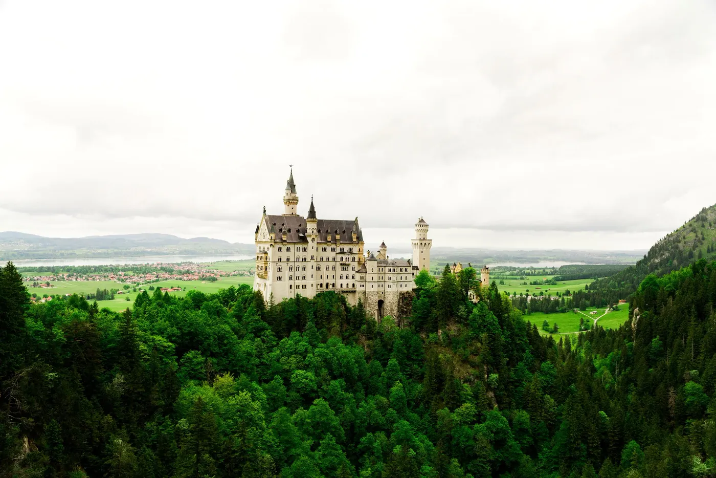 A turreted castle on a wooded hilltop above a broad green plain