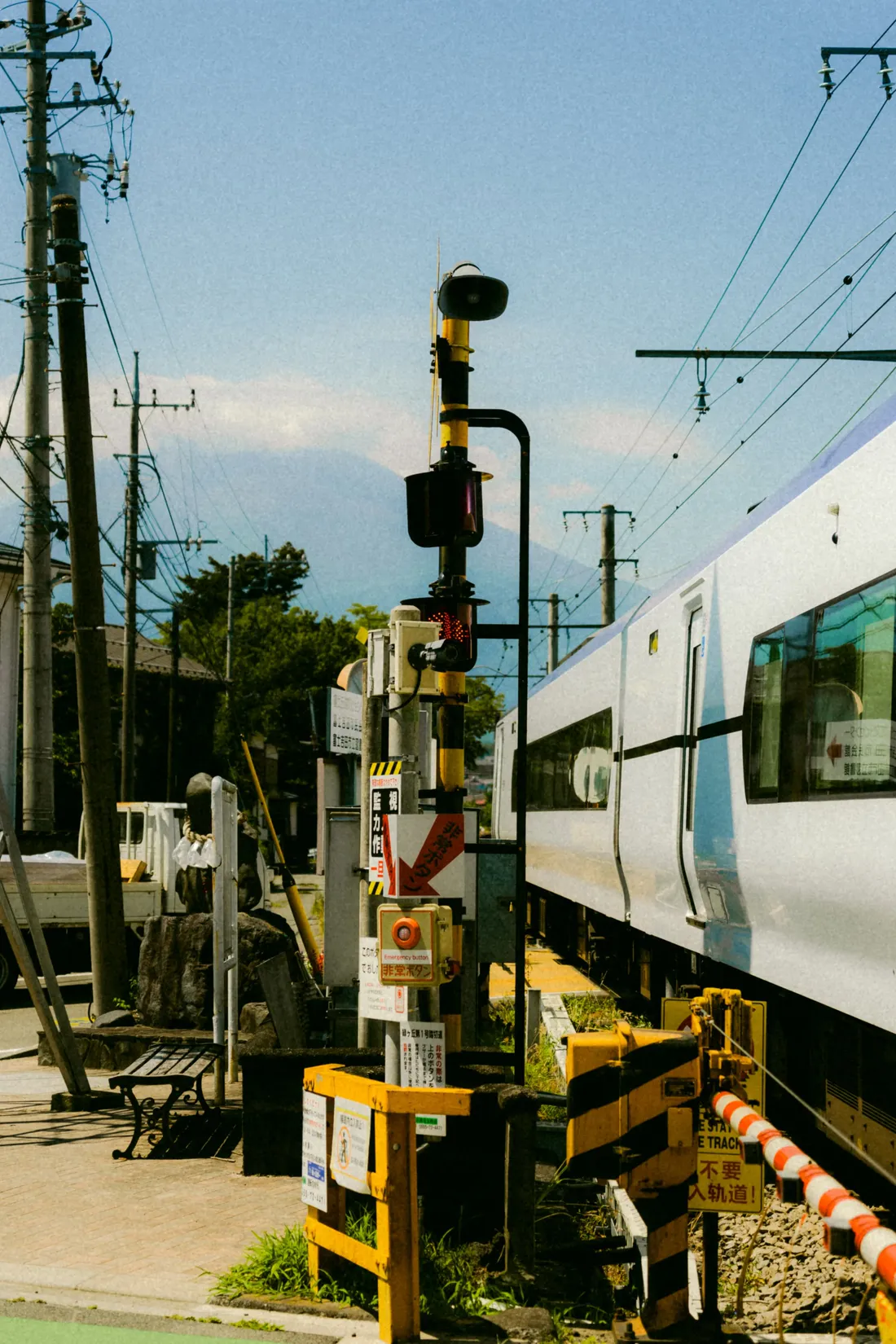 A train passing a level crossing beneath a tangle of poles and signals