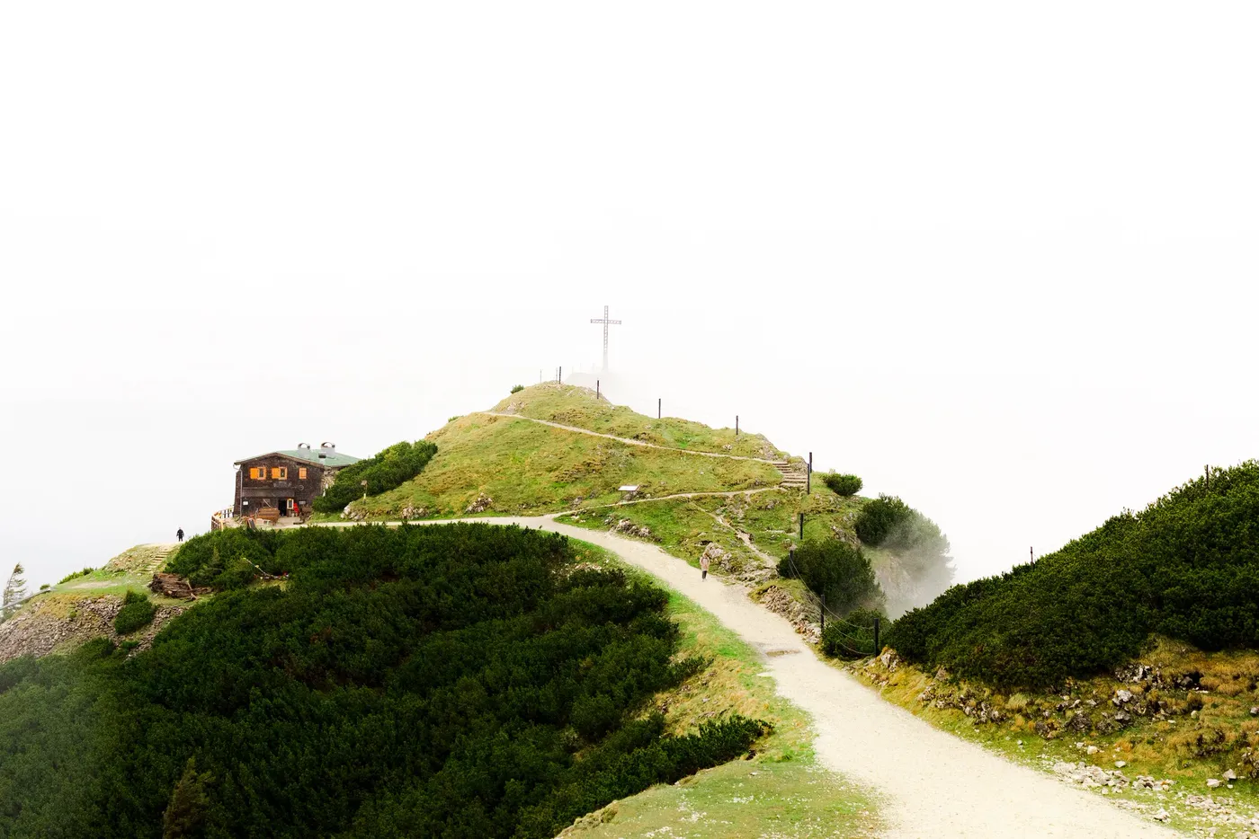 A gravel path climbing a grassy ridge toward a summit cross