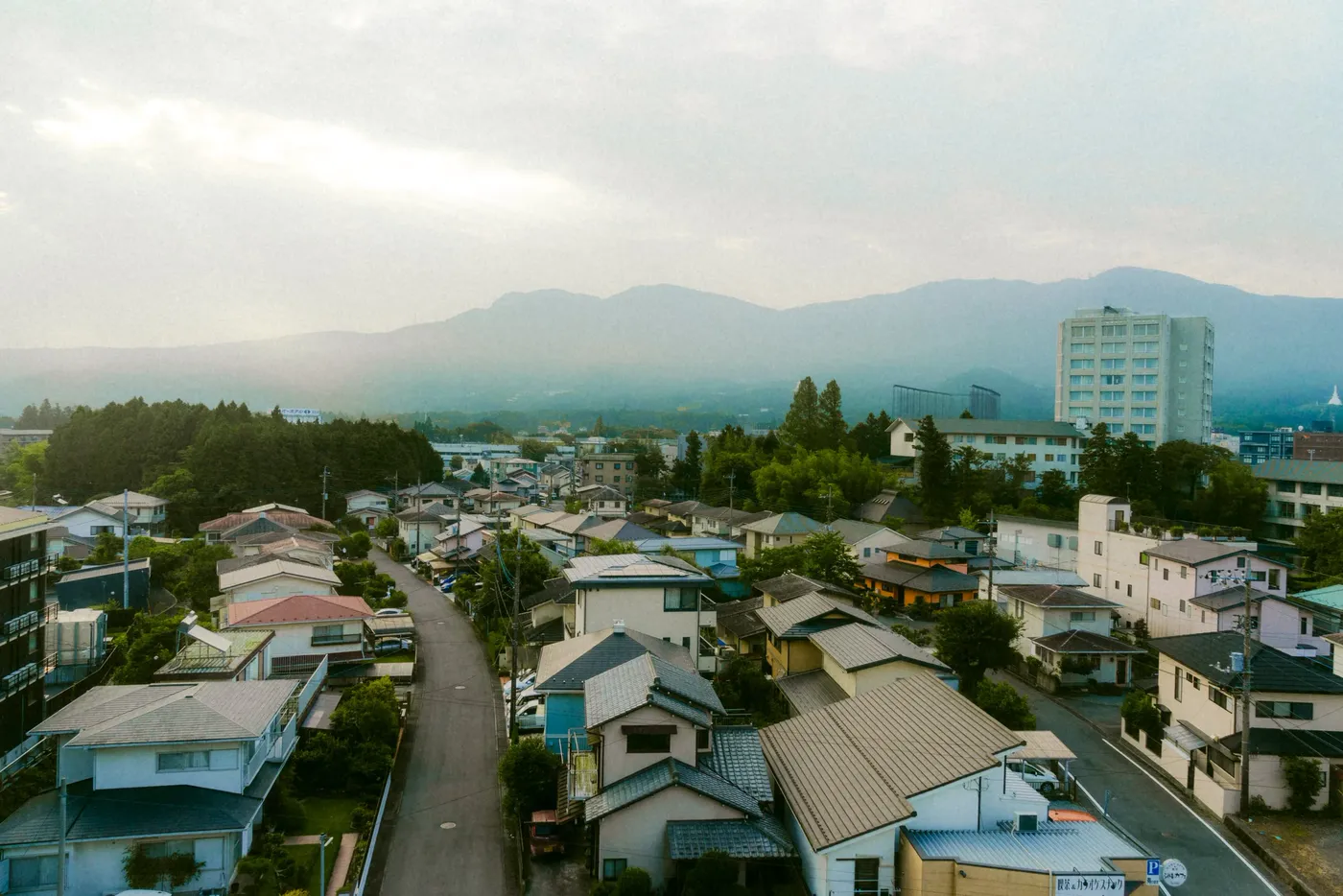 A hillside town of low rooftops under hazy distant mountains