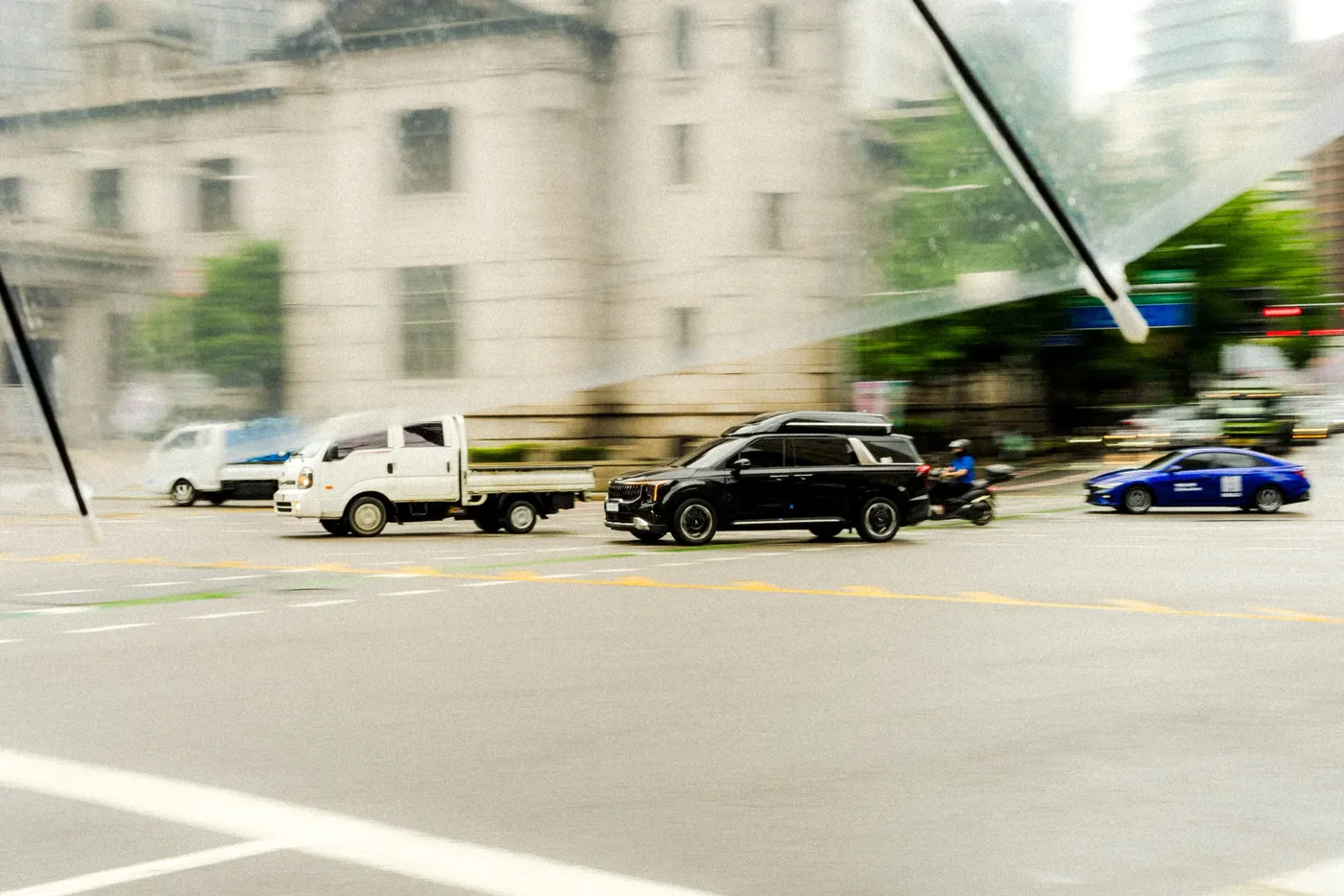 Trucks and cars streaking past a pale stone building in a long panning frame