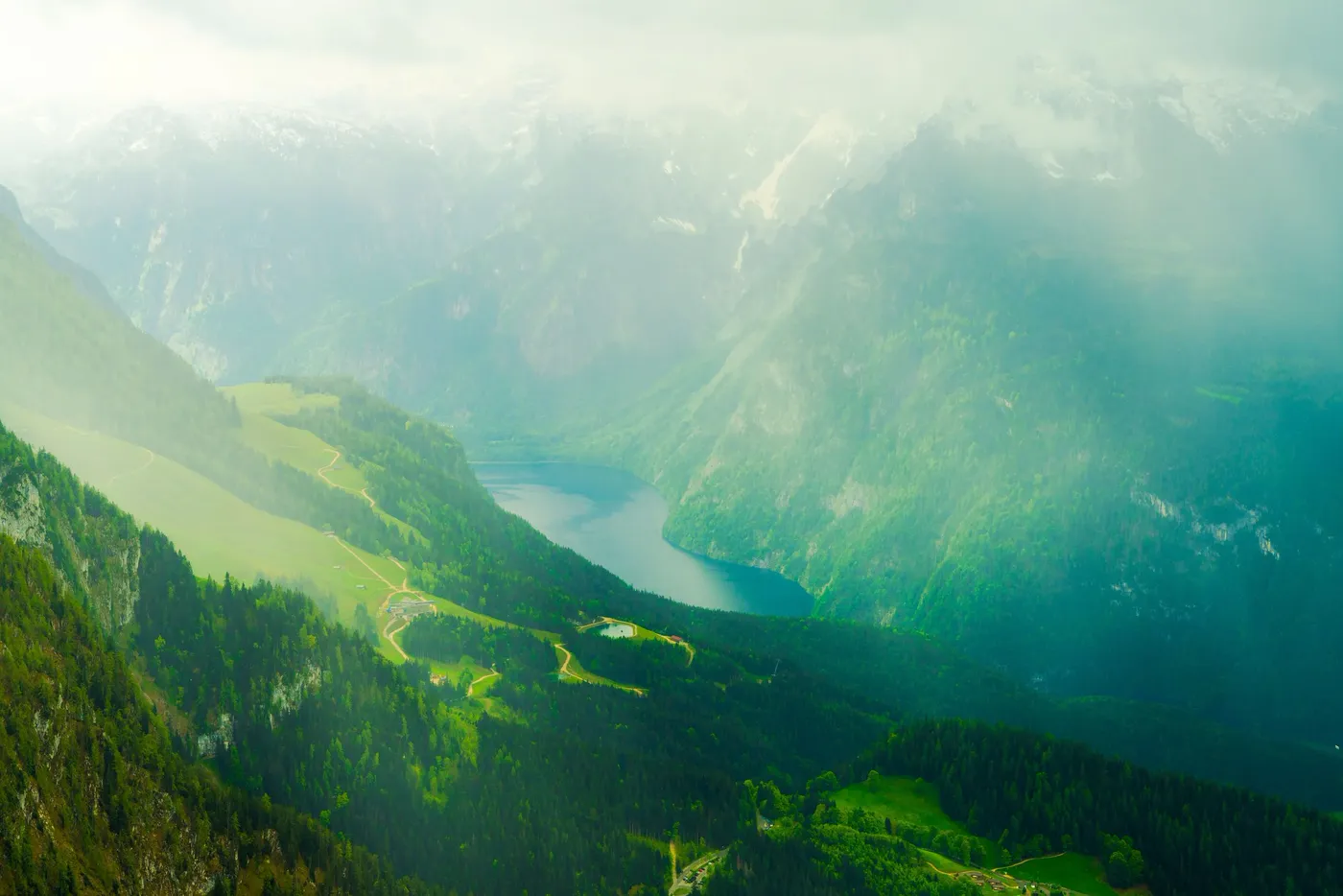 A green alpine valley and lake seen from high above, walls rising into haze