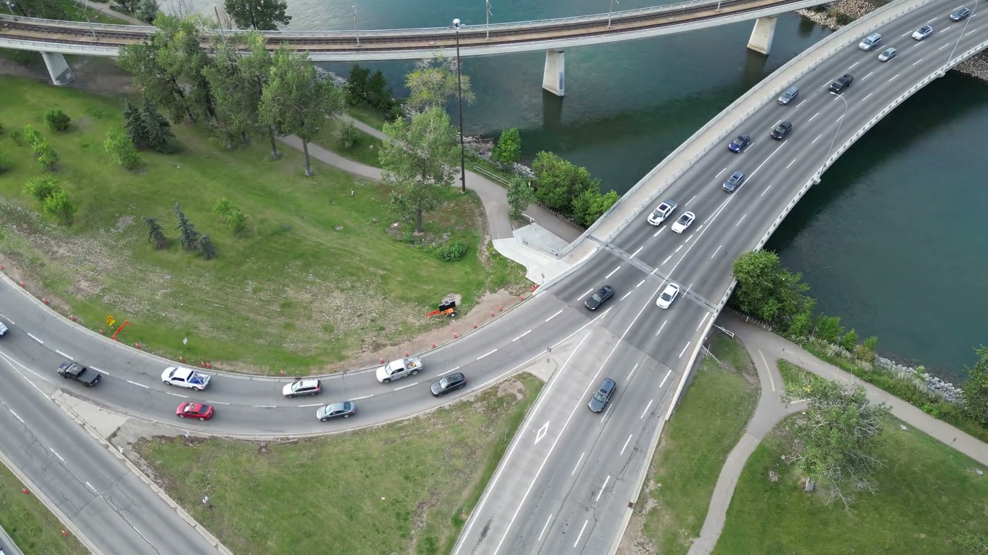 Directly above the Bow River at the Reconciliation Bridge: cars on the 1972 span, the CTrain bridge curving beside it, the riverside pathway between the two