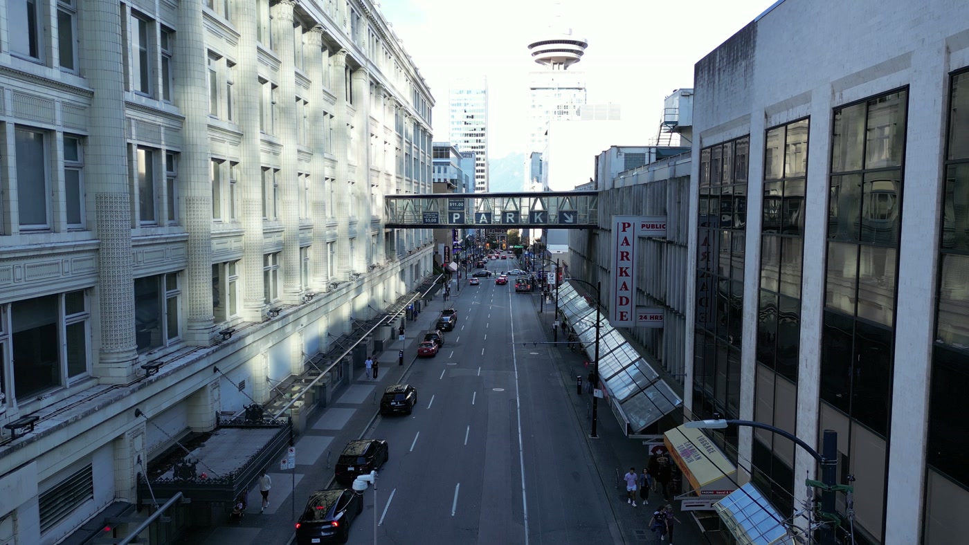 Seymour Street in Vancouver looking north over its 600 block: white terracotta on the left, the parkade's glass canopies and PARKADE sign on the right, the skybridge ahead, Harbour Centre's top beyond