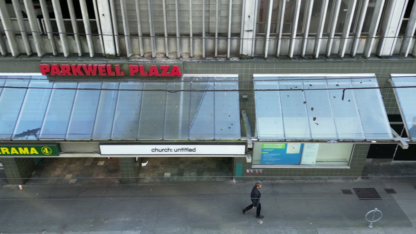 The white fascia reading church: untitled under a glass canopy on Seymour Street in Vancouver, the end of a DOLLARAMA sign to its left, PARKWELL PLAZA in red letters above, a passer-by below