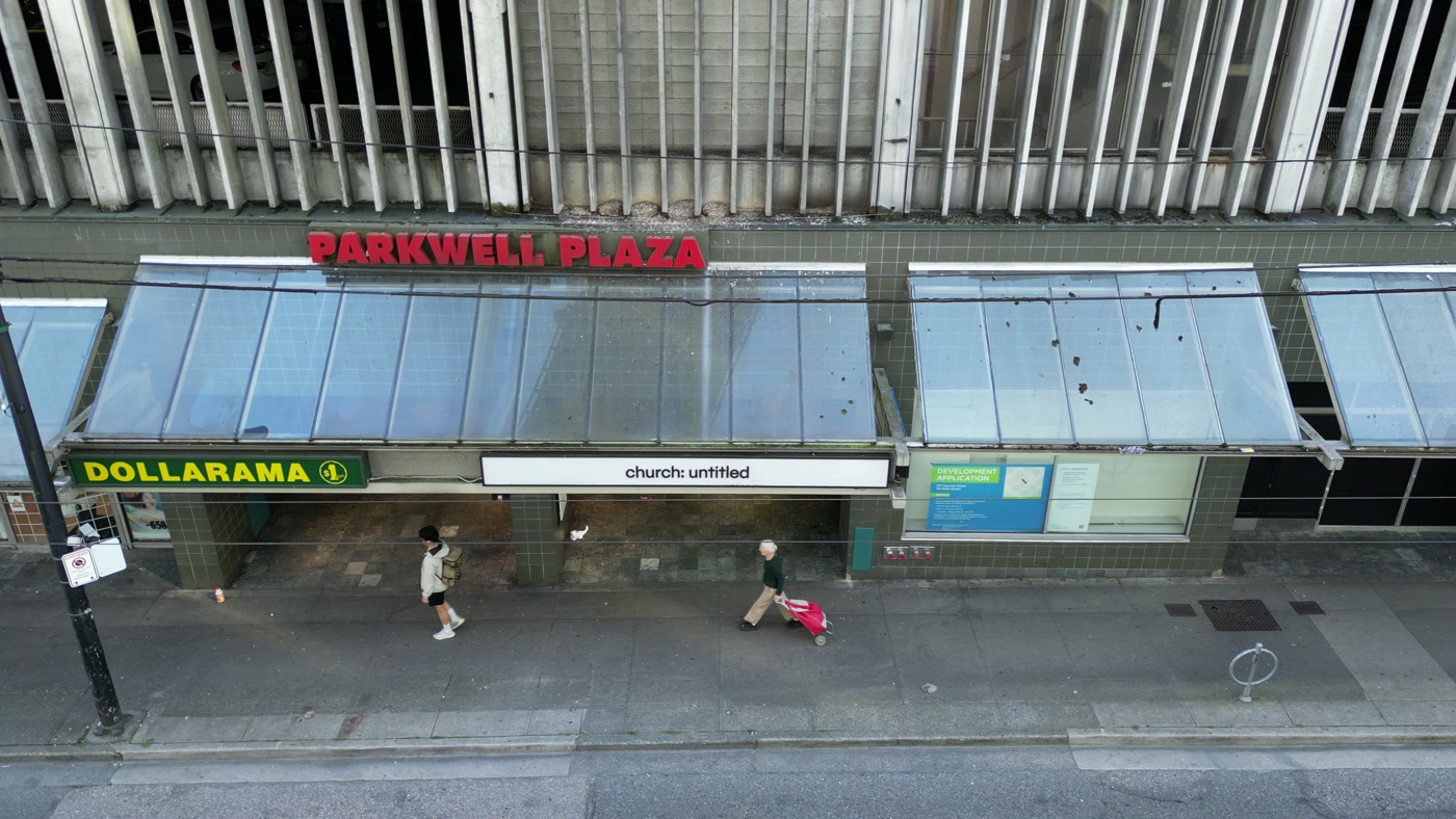 The storefront row at 110-668 Seymour Street, Vancouver: PARKWELL PLAZA over the glass canopies, the DOLLARAMA sign, the church: untitled fascia, someone pulling a pink suitcase along the sidewalk
