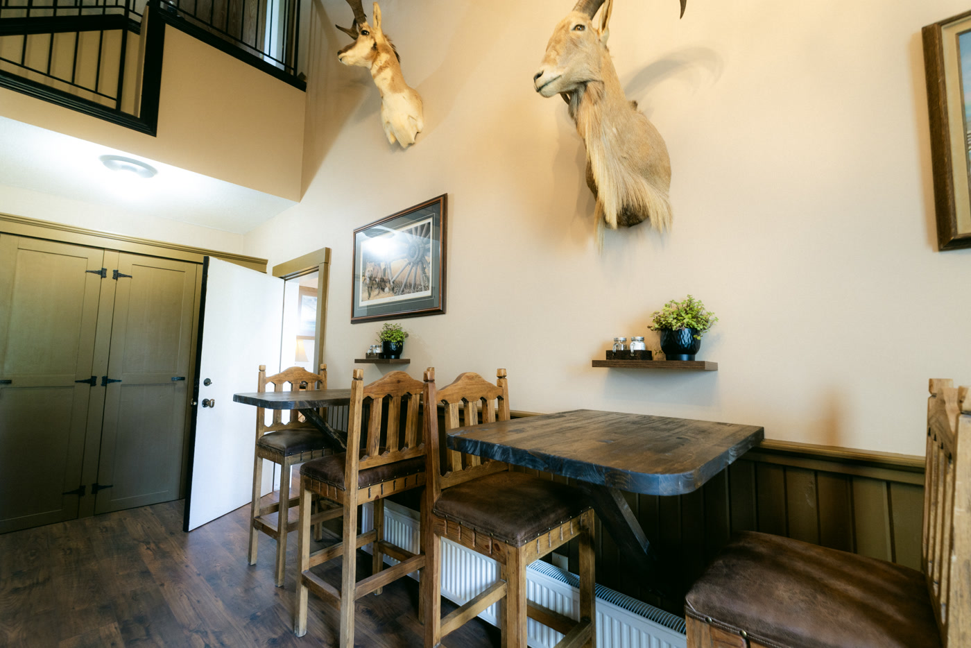 Wooden tables and tall carved chairs in the breakfast area of Shire Ridge Lodge near Bragg Creek, mounted heads on the wall above a shelf with a potted plant and green cabinet doors