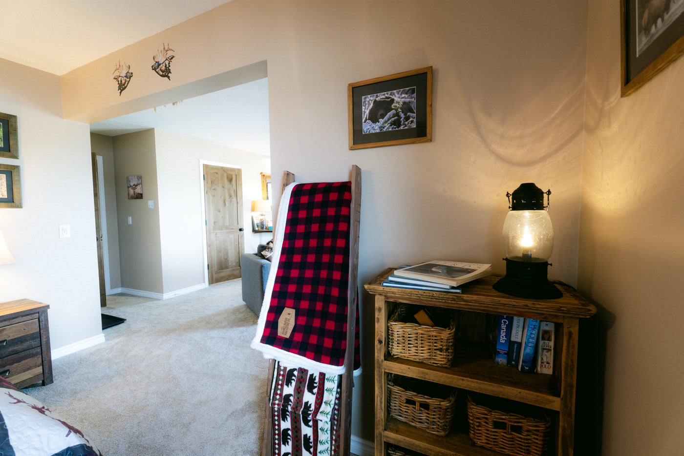 A plaid blanket over a wooden ladder, a bookshelf of baskets and a lantern lamp in the Elk Suite at Shire Ridge Lodge near Bragg Creek, a framed bear print on the wall