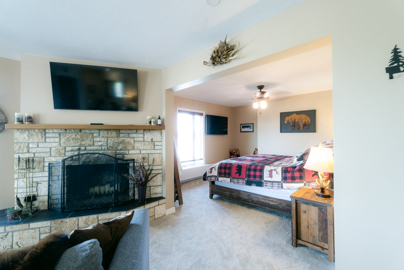 The stone fireplace in the Elk Suite at Shire Ridge Lodge near Bragg Creek, a television and antler decor above its mantel, the plaid-covered bed visible through the opening beside it