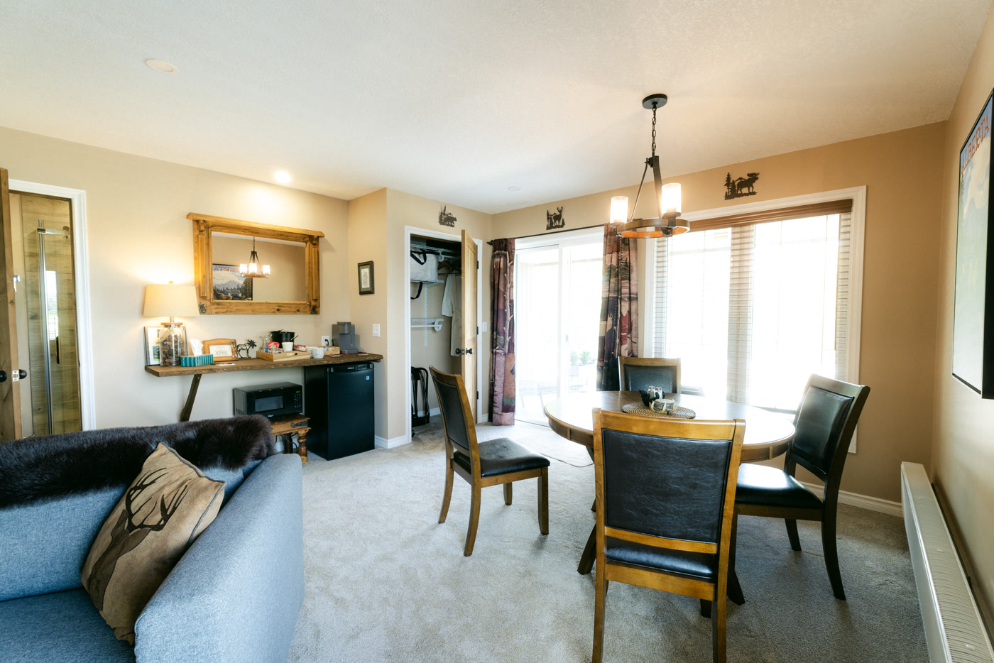 The Elk Suite at Shire Ridge Lodge near Bragg Creek from the sofa: the round dining table and chairs, a desk with a mirror, a small chandelier and windows onto the balcony