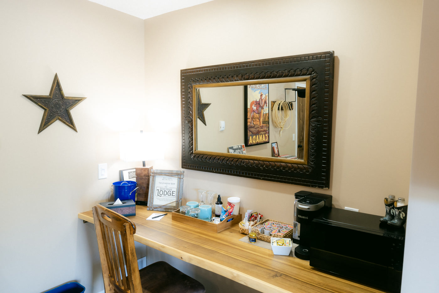 The desk nook in the Stampede Room at Shire Ridge Lodge near Bragg Creek: a wooden counter under a heavy framed mirror, a coffee machine, a tray of snacks and a metal star
