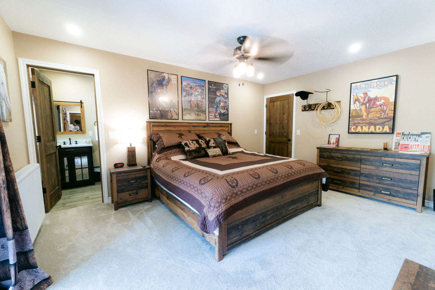 The Stampede Room from its corner at Shire Ridge Lodge near Bragg Creek: the bed, the Stampede posters, the Alberta Canada poster above a long dresser, and the bathroom door open