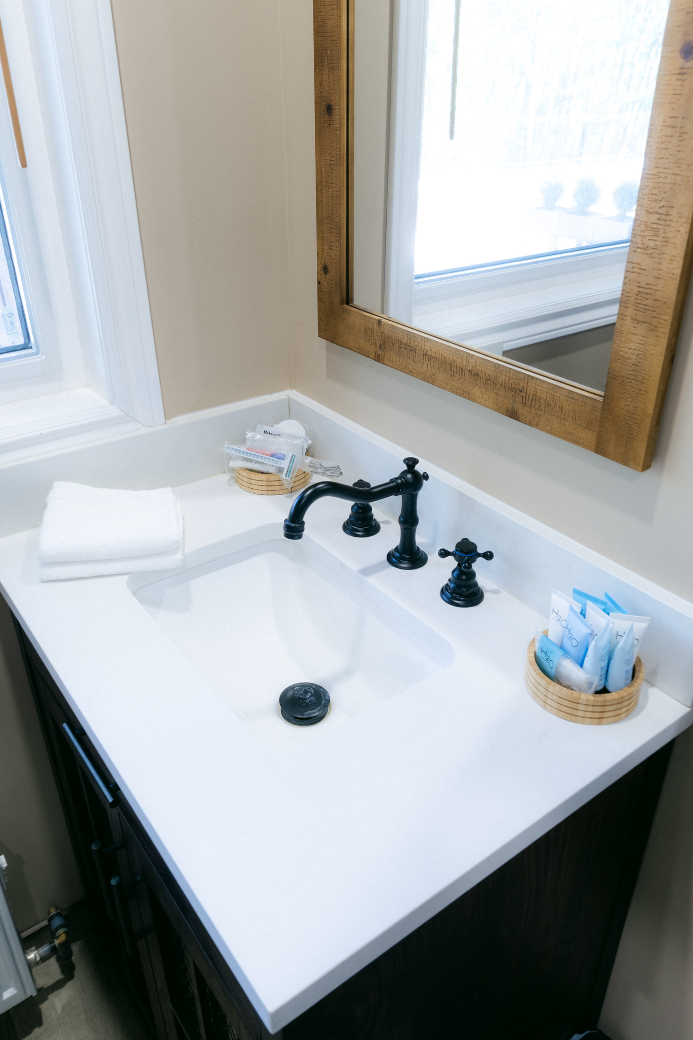 The Stampede Room's vanity at Shire Ridge Lodge near Bragg Creek close up: a white basin with a black faucet, folded towels, a basket of toiletries and a wood-framed mirror