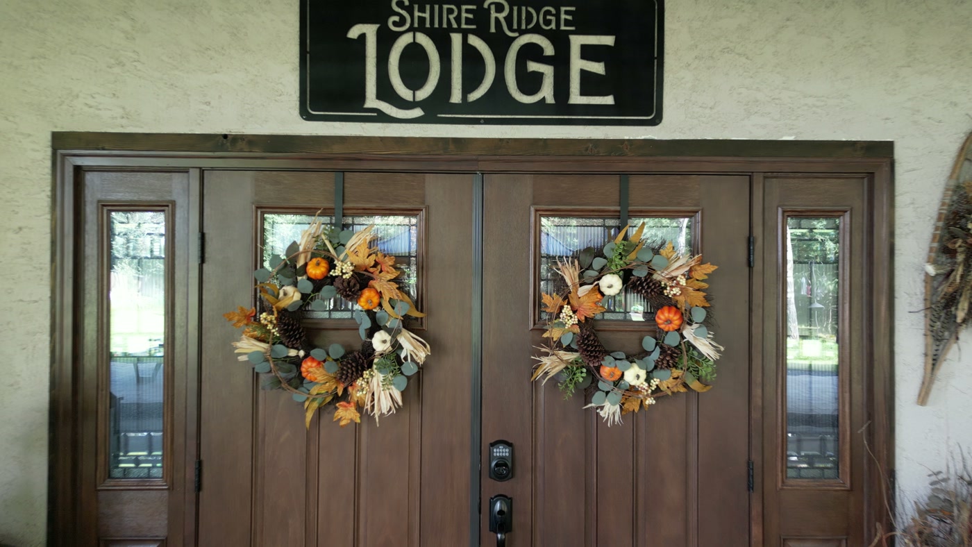 The front doors of Shire Ridge Lodge near Bragg Creek: the black Shire Ridge Lodge sign above double wooden doors hung with autumn wreaths of eucalyptus, pumpkins, pinecones and corn husks