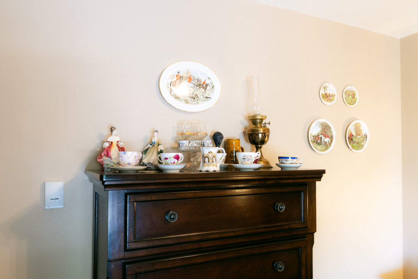 Antique china on a dark dresser in the Windsor Room at Shire Ridge Lodge near Bragg Creek: teacups, figurines, a royal commemorative jug, a brass oil lamp, and plates hung above