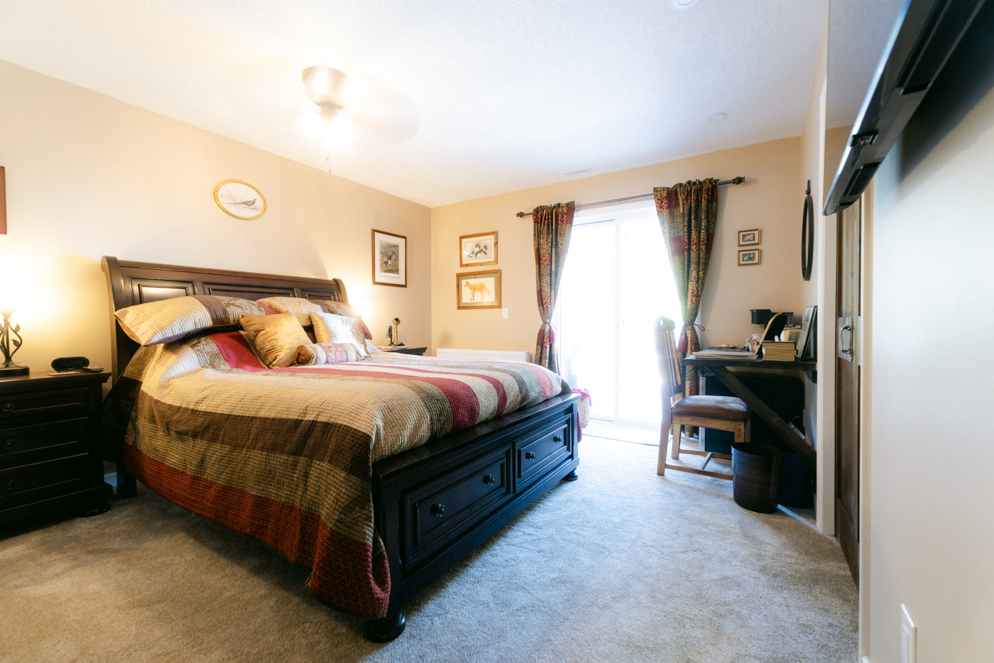 The Windsor Room at Shire Ridge Lodge near Bragg Creek: a dark sleigh bed with a striped quilt and cushions, framed prints and a plate on the wall, curtained windows and a desk