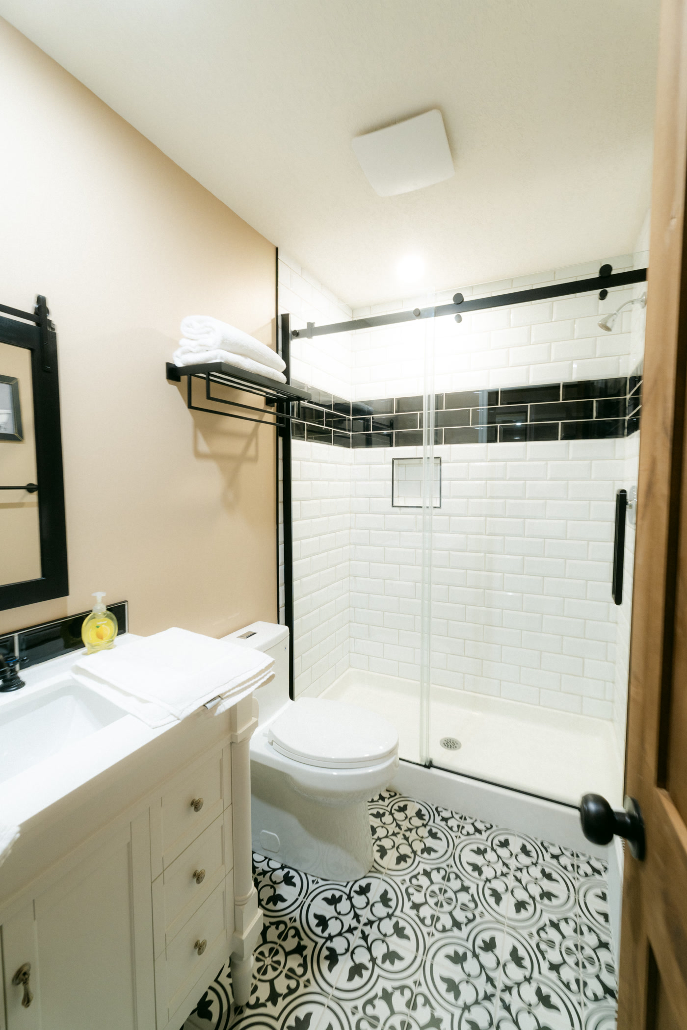 The Windsor Room's bathroom at Shire Ridge Lodge near Bragg Creek: a white subway-tile walk-in shower trimmed in black, a white vanity and a black-and-white patterned tile floor