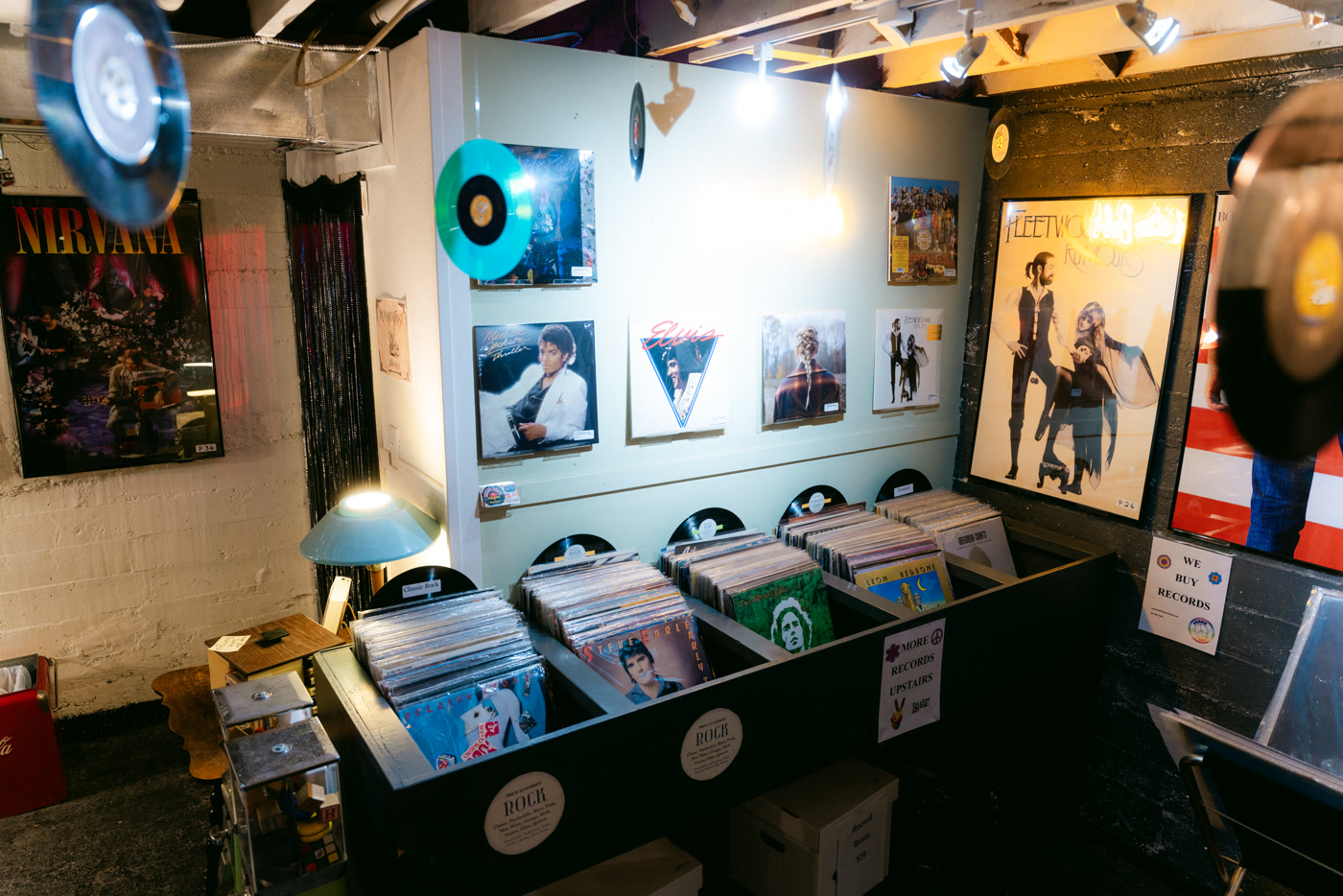 Record bins under framed posters and records hung on white brick in the downstairs room at Found Books & Shop in Cochrane