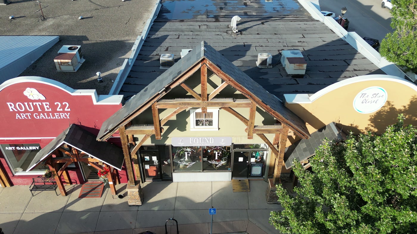 Route 22 Art Gallery's red sign and the timber gable of Found Books & Shop side by side in the same row on 1st Street West in Cochrane