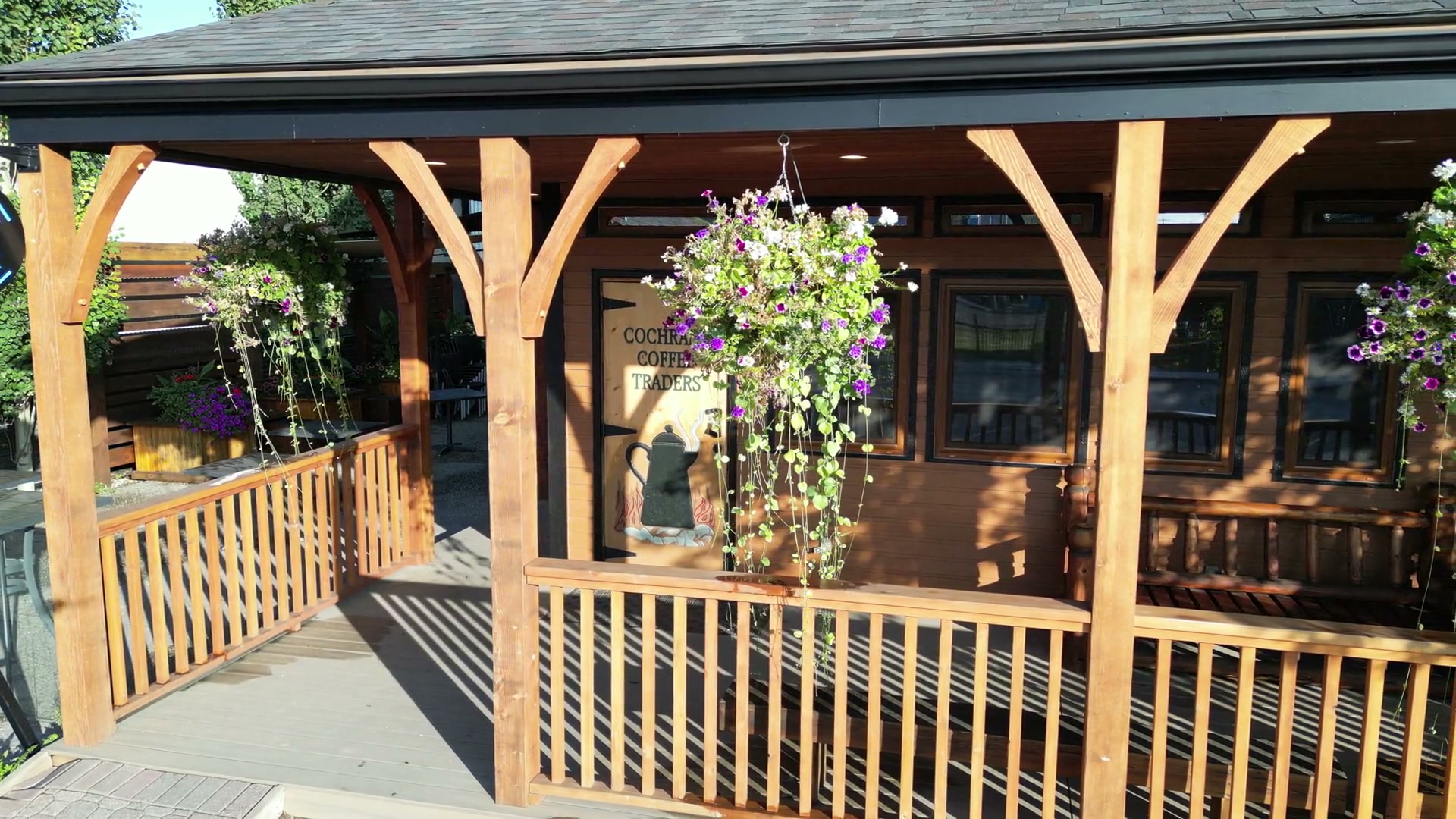 The timber porch of Cochrane Coffee Traders held nearly head-on: curved braces on square posts, a rail of plain spindles, hanging baskets of purple and white flowers, and the painted door between them