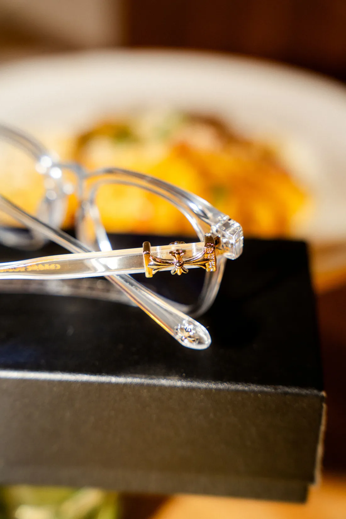 Clear acetate eyeglasses resting on a black box beside a plate of food