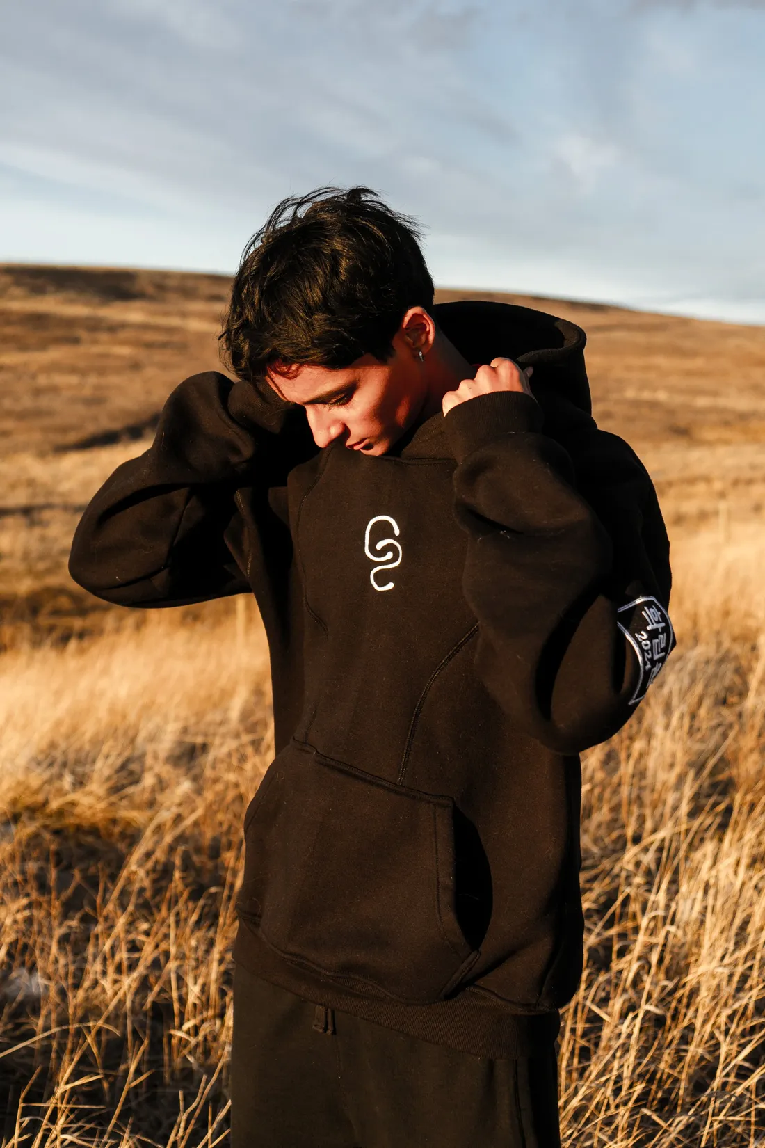 A person pulling a brown hoodie hood up in a field of dry golden grass