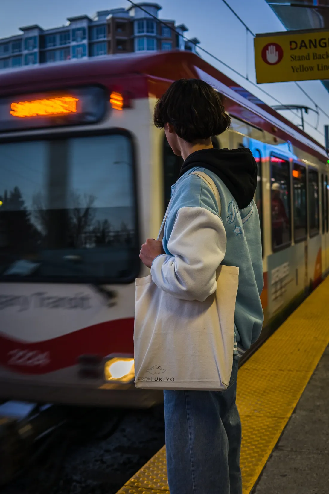 A person with a canvas tote waiting on a light-rail platform as the train pulls in
