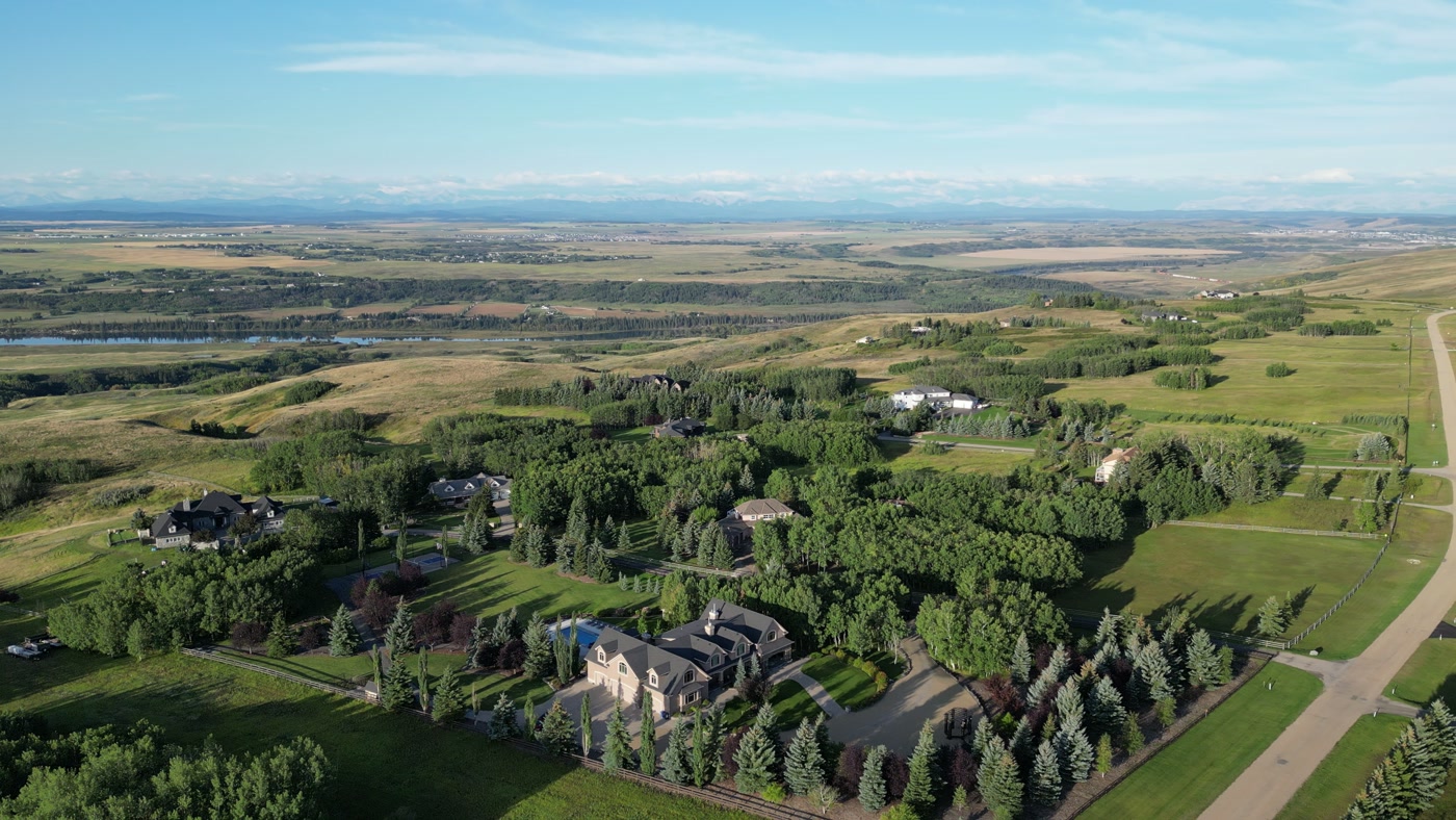 Open Alberta country stretching to the Rockies beyond the estate's trees — road, river, property and mountains in one frame from altitude