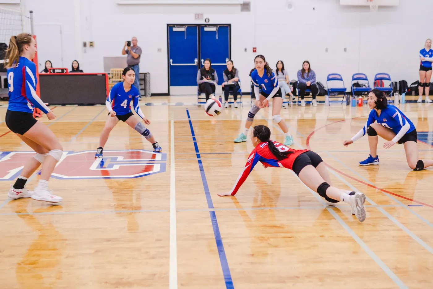 A volleyball player diving flat to the floor for a dig as teammates set behind her