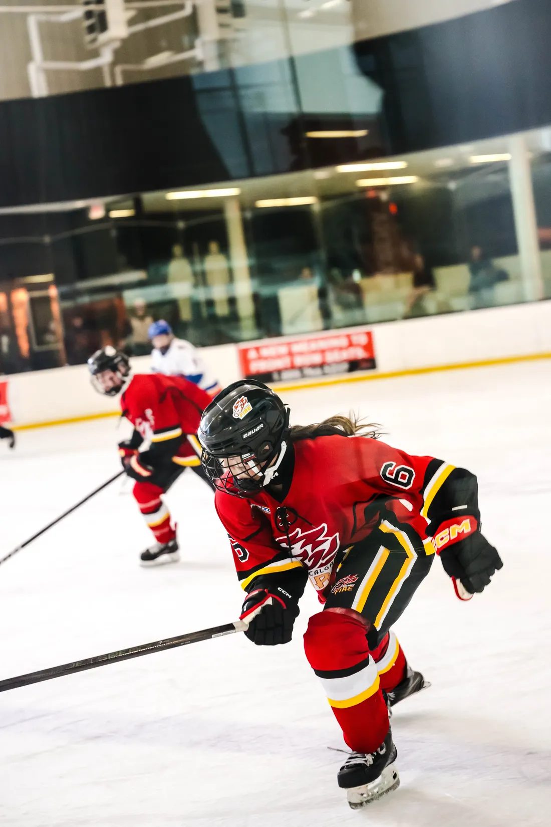 A hockey player in a red jersey and cage skating hard through the neutral zone with an opponent behind