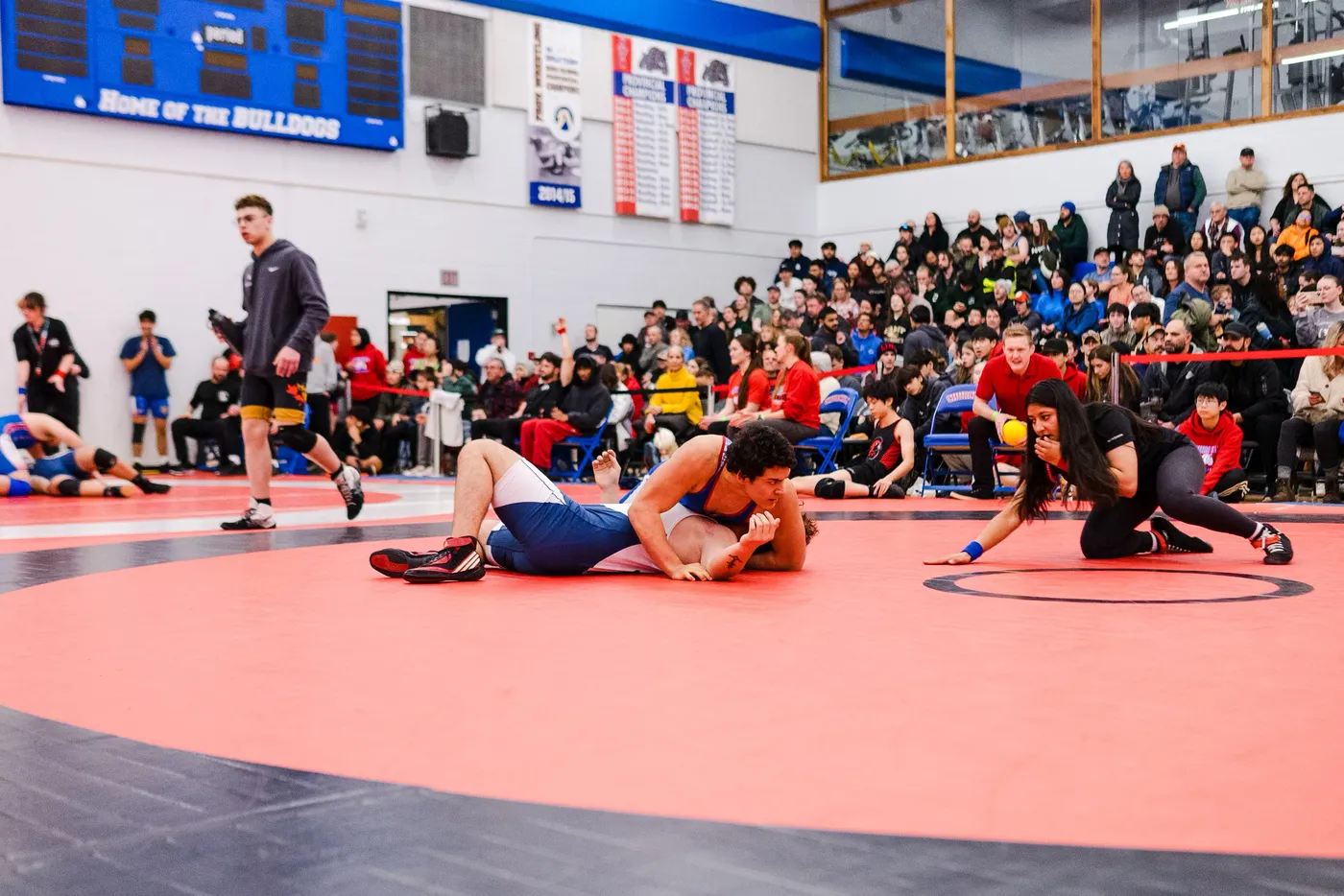 Two wrestlers locked on the mat in front of a packed gymnasium crowd