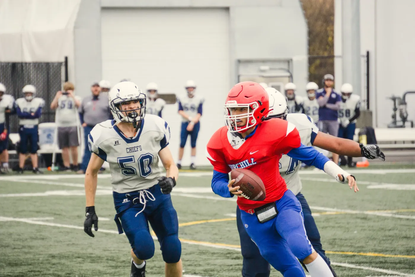 A quarterback in a red jersey turning with the ball as a defender closes in on an indoor field