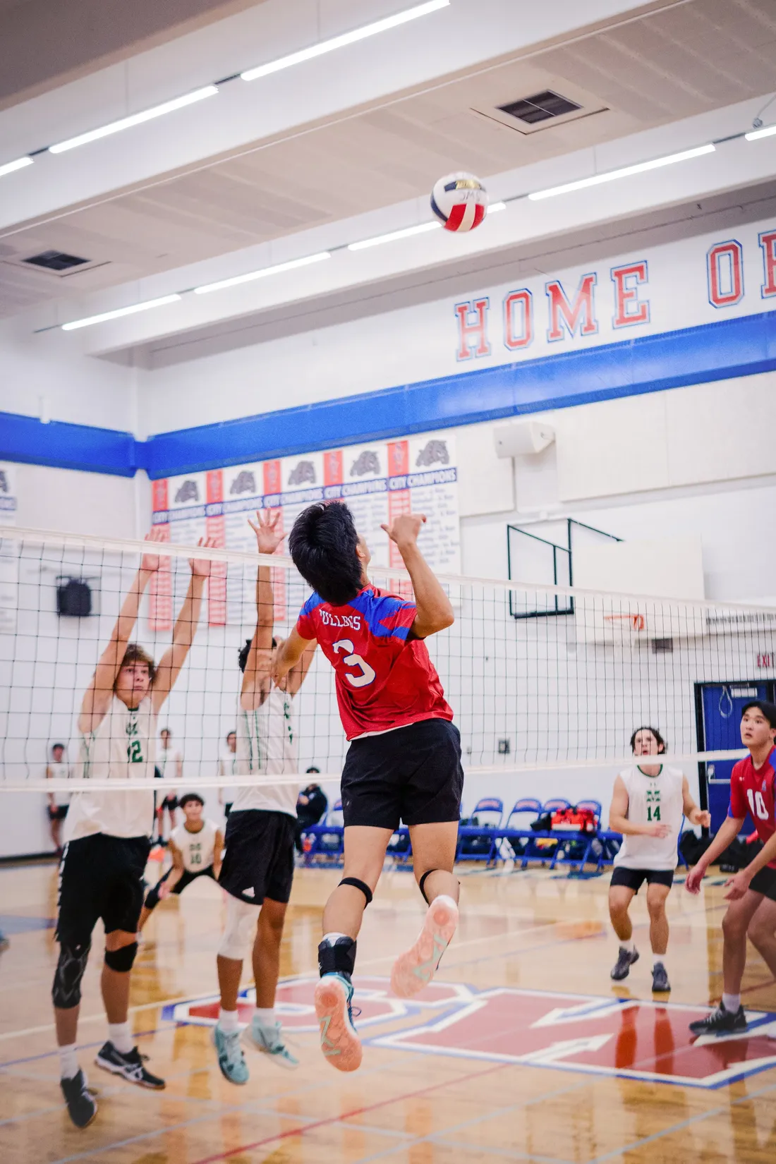 Volleyball players at the net as the ball hangs above them in a school gymnasium