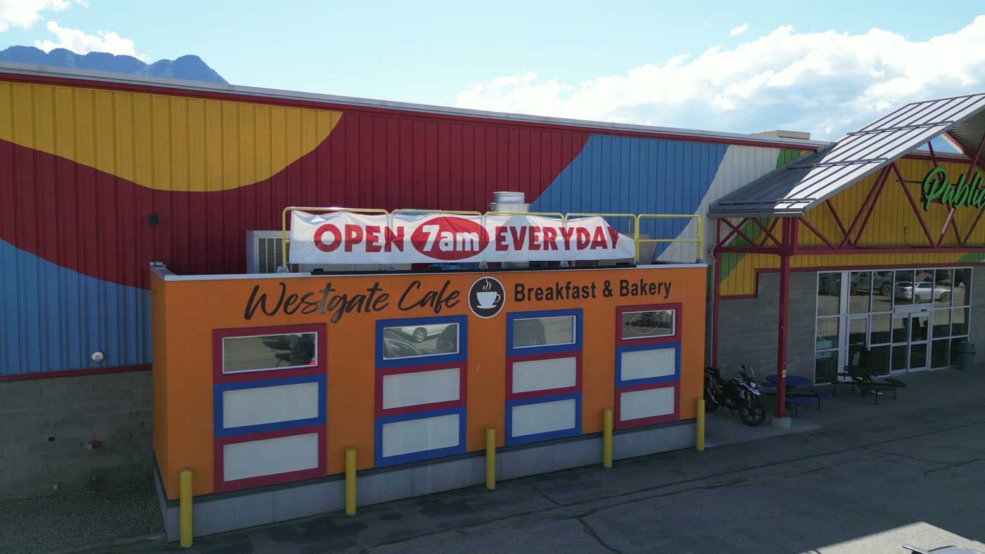 Westgate Cafe three-quarters on in Salmon Arm: the orange front, its banner and four framed windows against the painted wall, a motorcycle by the door, and the market's red steel gable