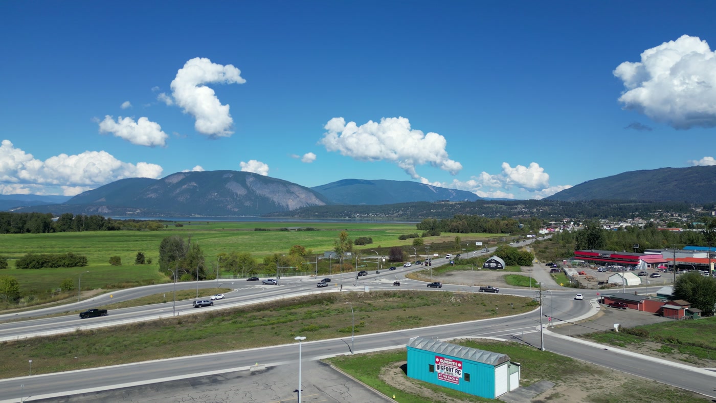 From above Westgate Public Market in Salmon Arm, looking past a teal hut and across the highway to green fields, the edge of town, and Shuswap Lake under the far hills