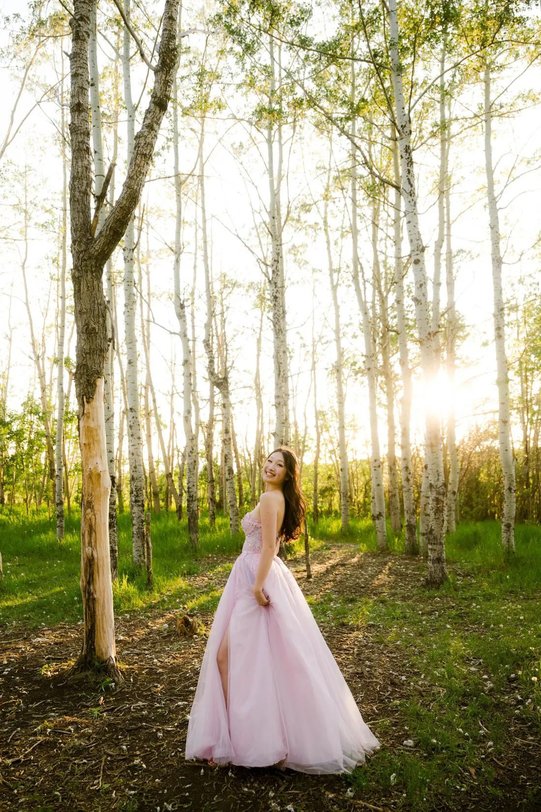 A woman in a pale pink gown in a backlit aspen grove at golden hour