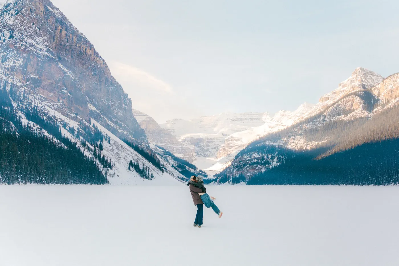 A couple embracing in the middle of a frozen lake ringed by snow-covered peaks