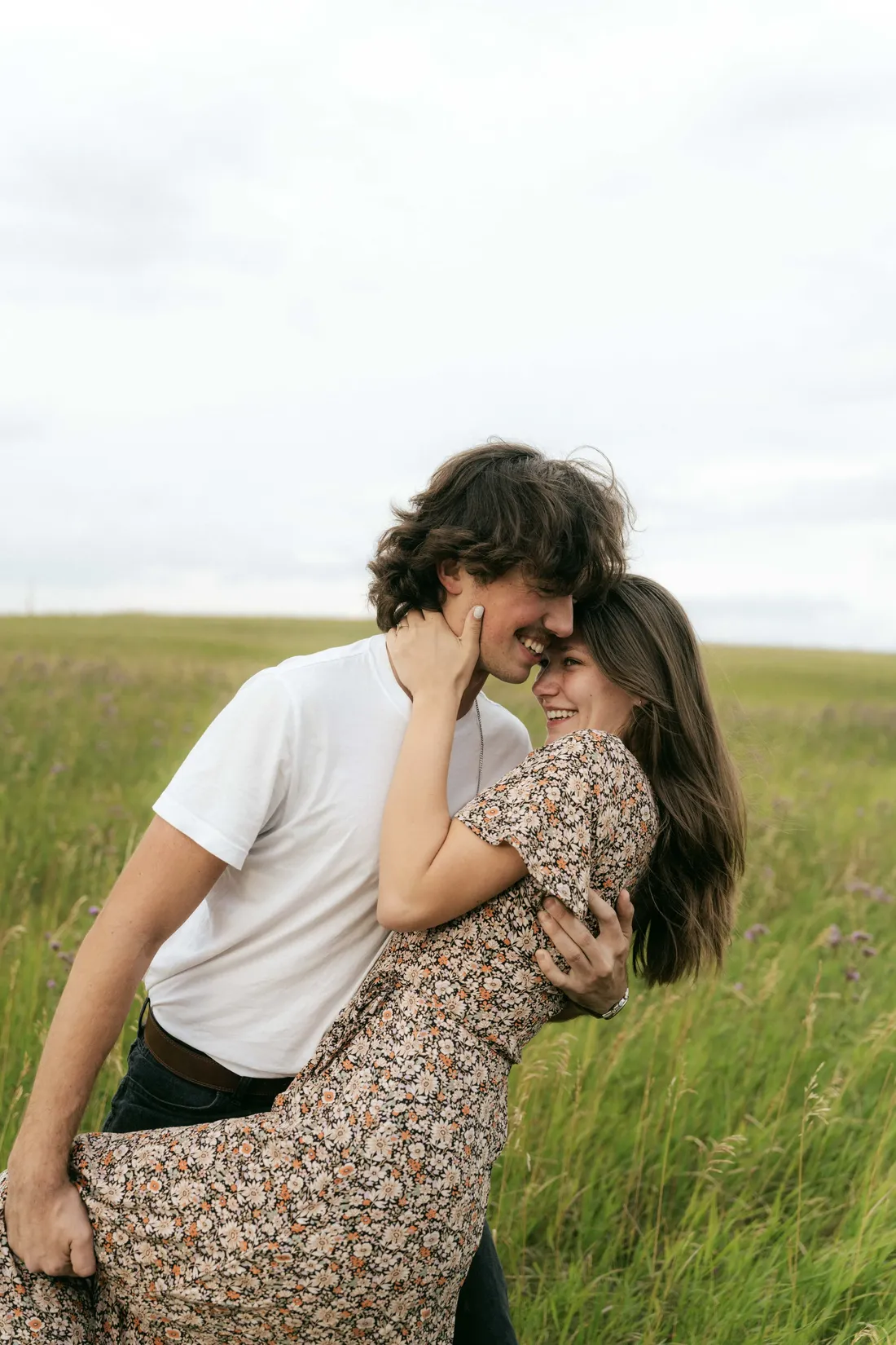 A couple embracing in waist-high prairie grass, her hand at his face