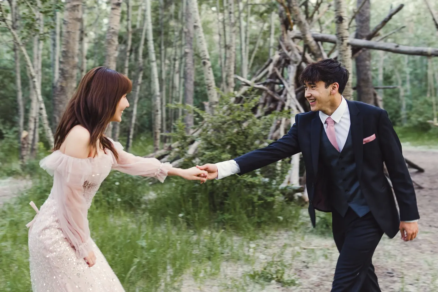 A couple in formal dress reaching for each other's hands on an aspen woodland path