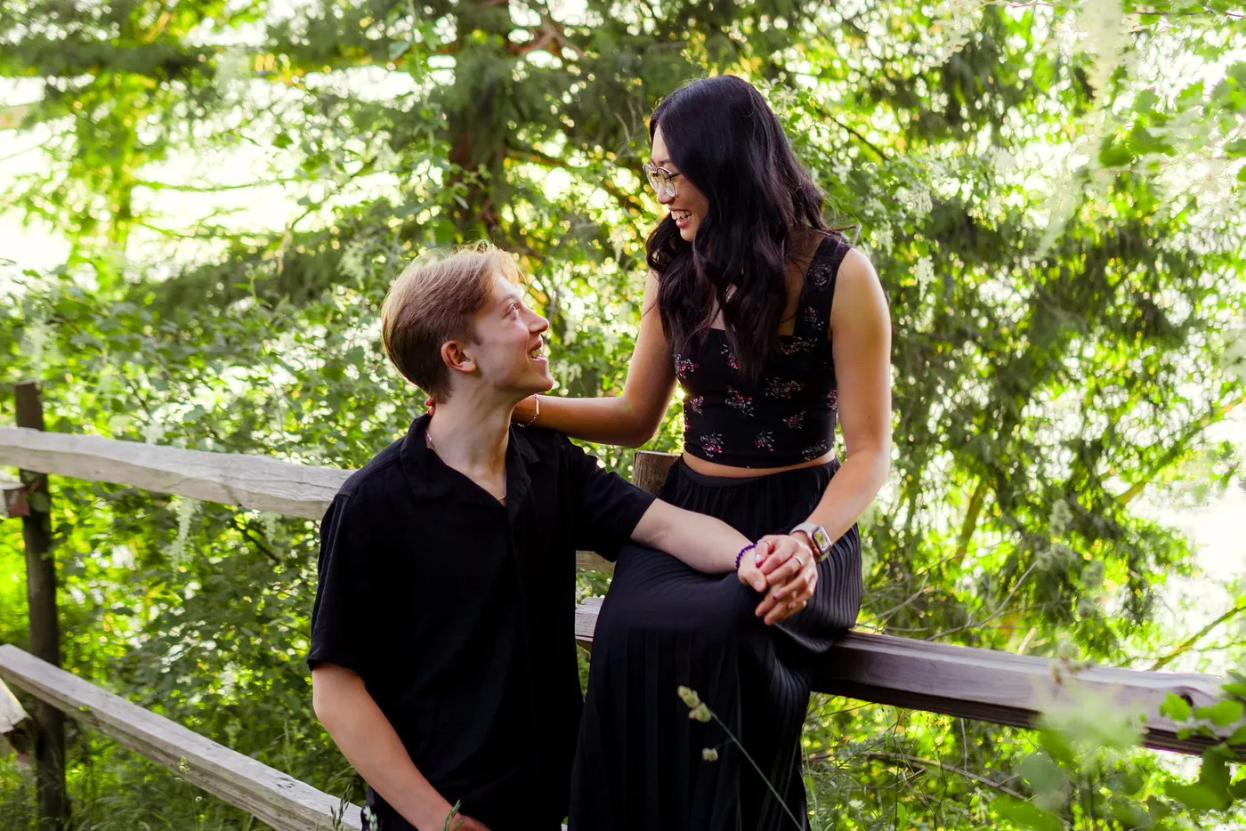 A couple laughing together on a wooden garden fence rail surrounded by green