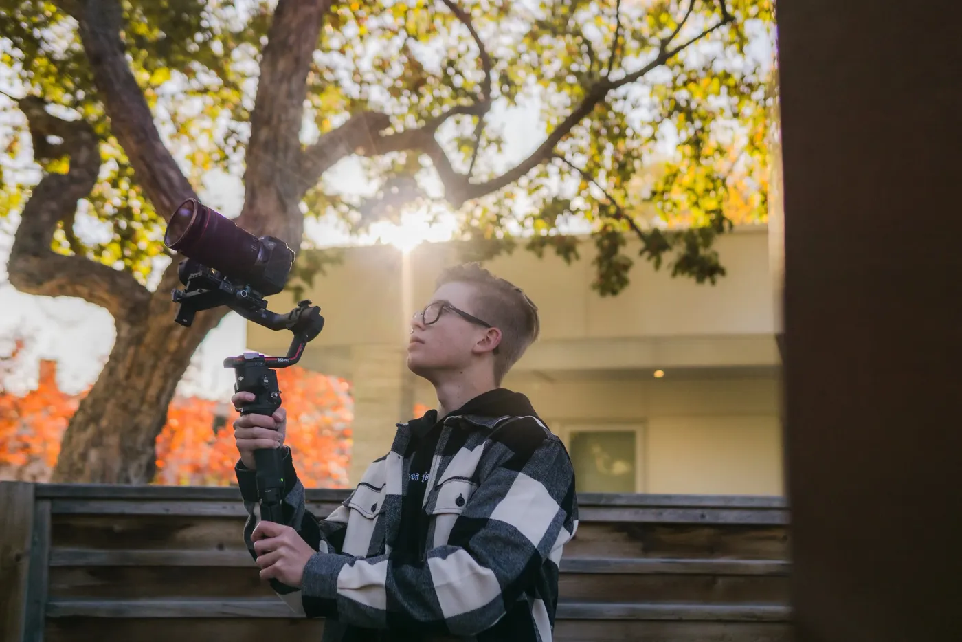 A videographer holding a gimbal-mounted camera under an autumn tree