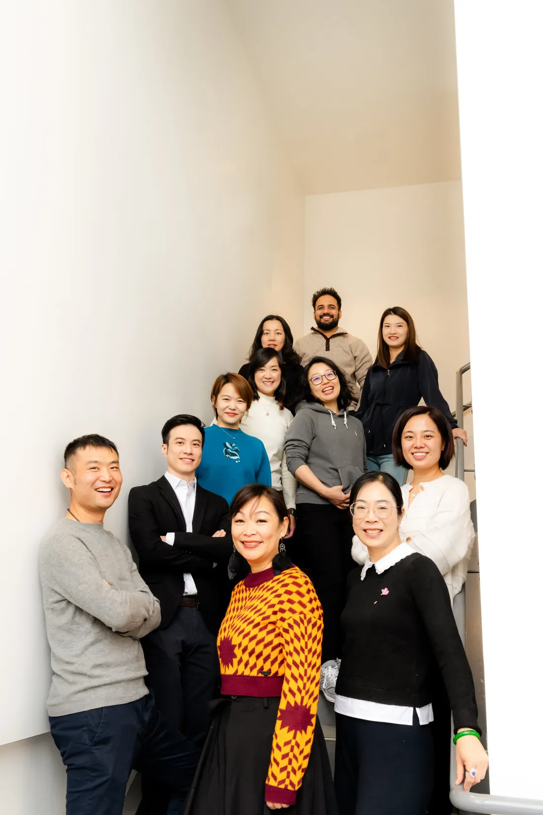 A large team gathered on a bright office stairwell for a group portrait