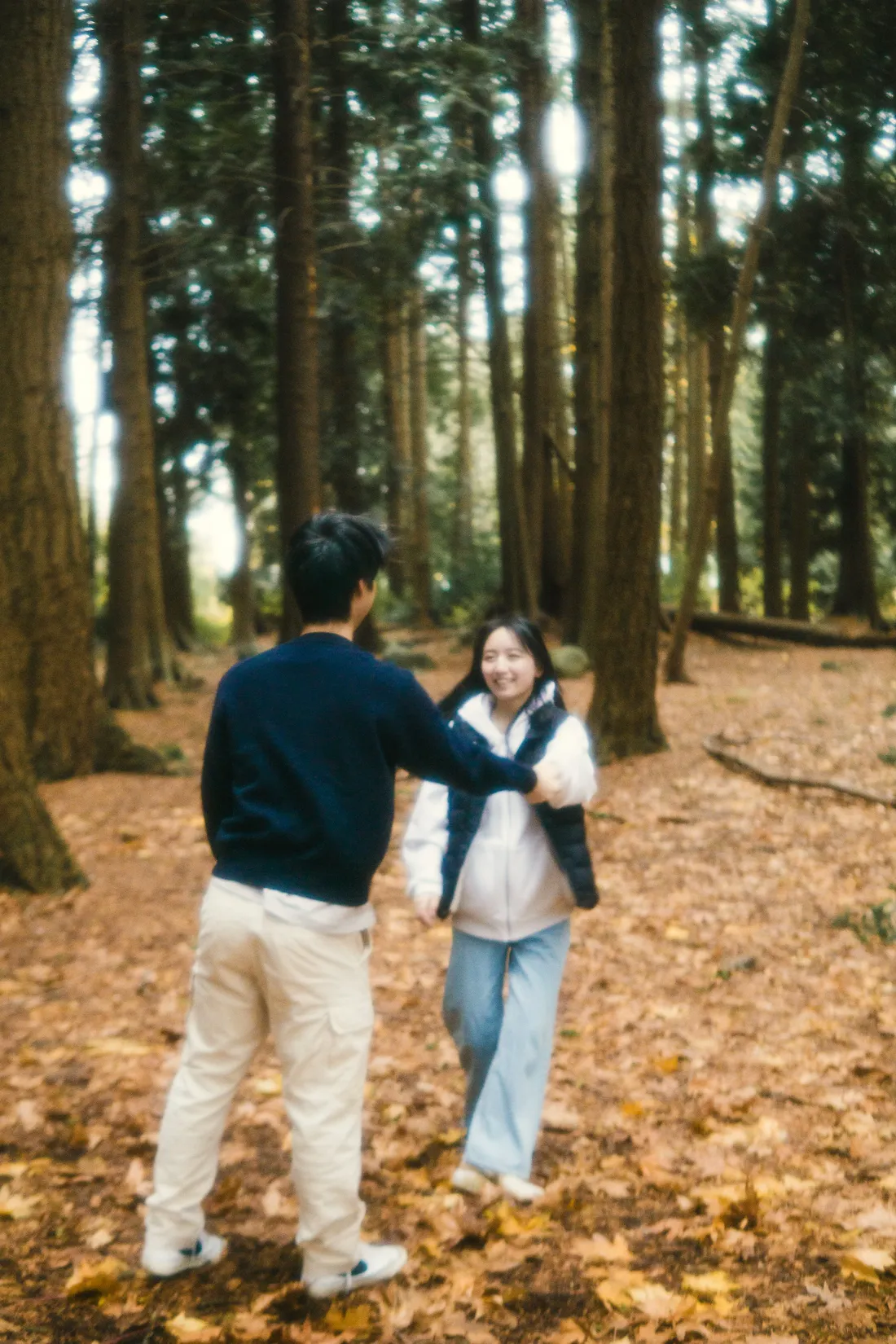 A couple turning toward each other on a forest floor covered in fallen leaves