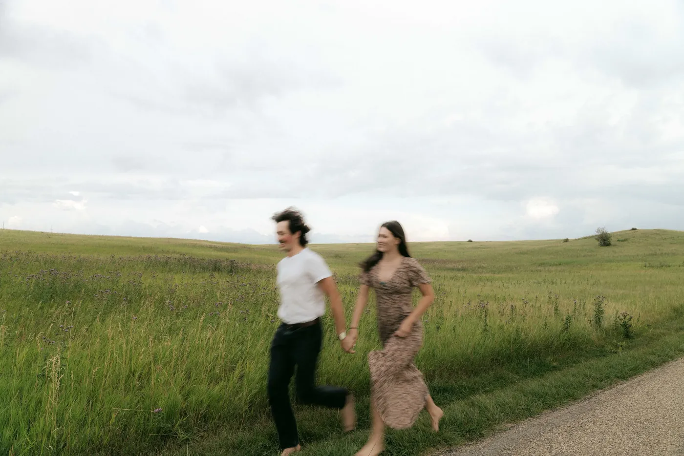 A couple walking hand in hand along a gravel path through rolling prairie